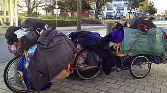 Obdachloser mit Fahrrad und viel Hausrat in Tüten und Taschen