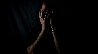 Frau im Dunkeln verbirgt ihr Gesicht hinter den Händen.