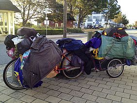 Obdachloser mit Fahrrad und viel Hausrat in Tüten und Taschen