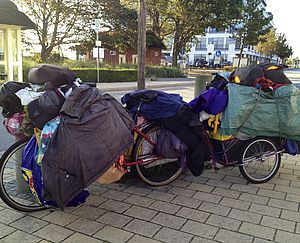 Obdachloser mit Fahrrad und viel Hausrat in Tüten und Taschen