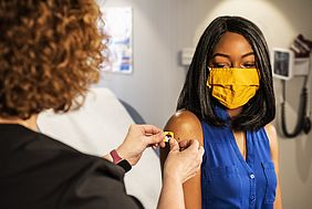 Arzthelferin klebt Patientin nach Impfung ein Pflaster auf.